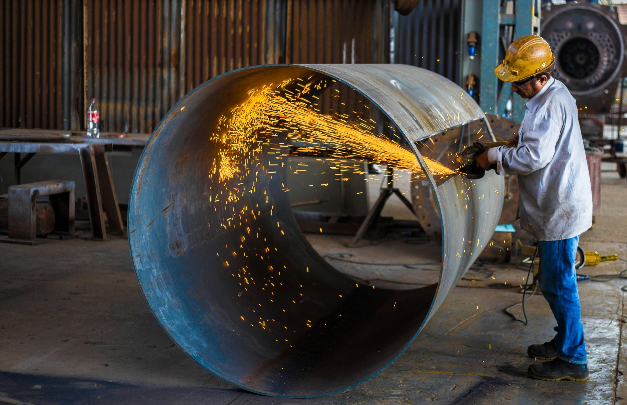 Worker using a grinder on a large metal cylinder, illustrating the industrial applications of boride compounds.