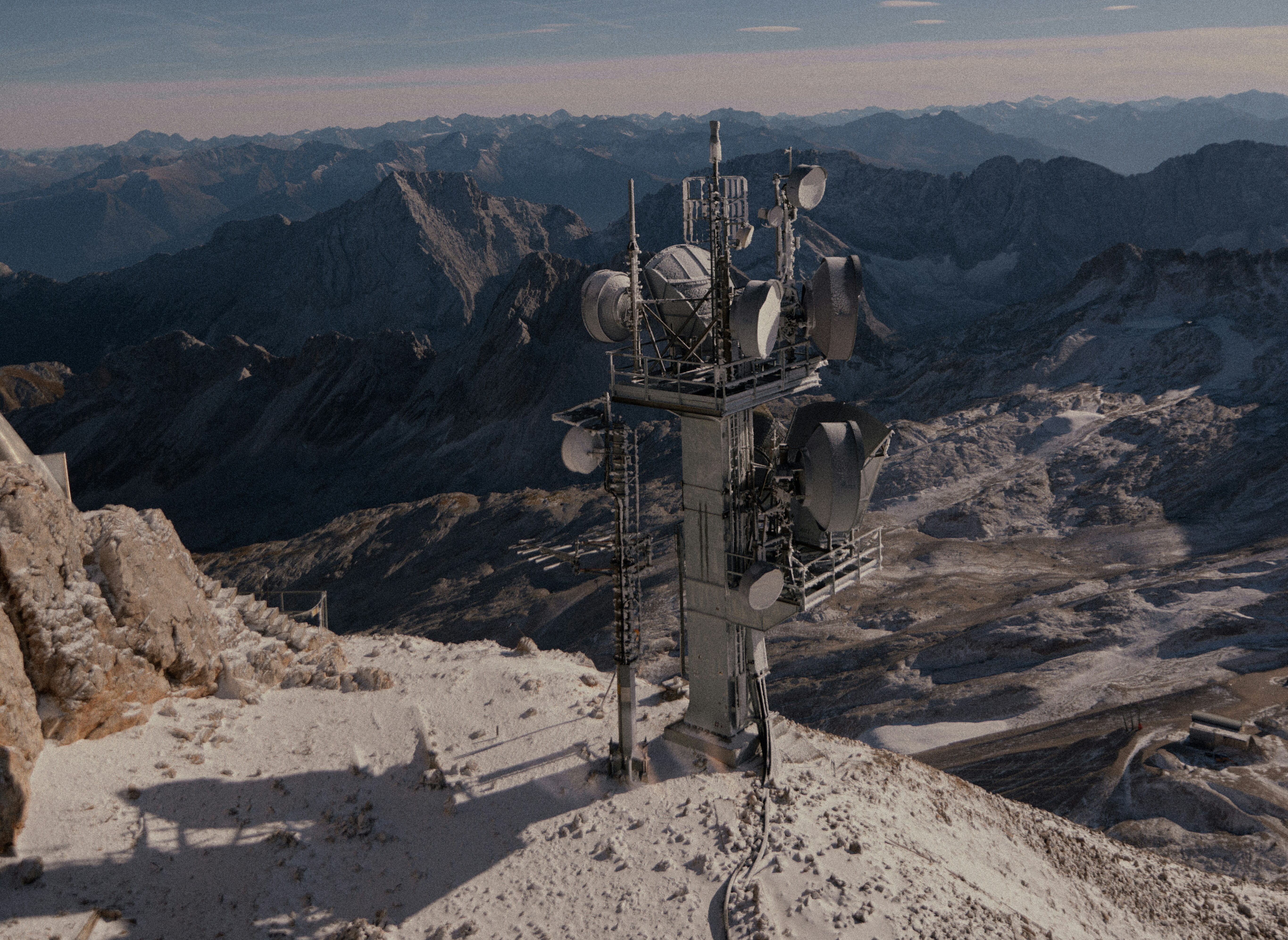 A satellite communication tower on a snowy mountain peak, with vast mountain ranges in the background under a clear sky.