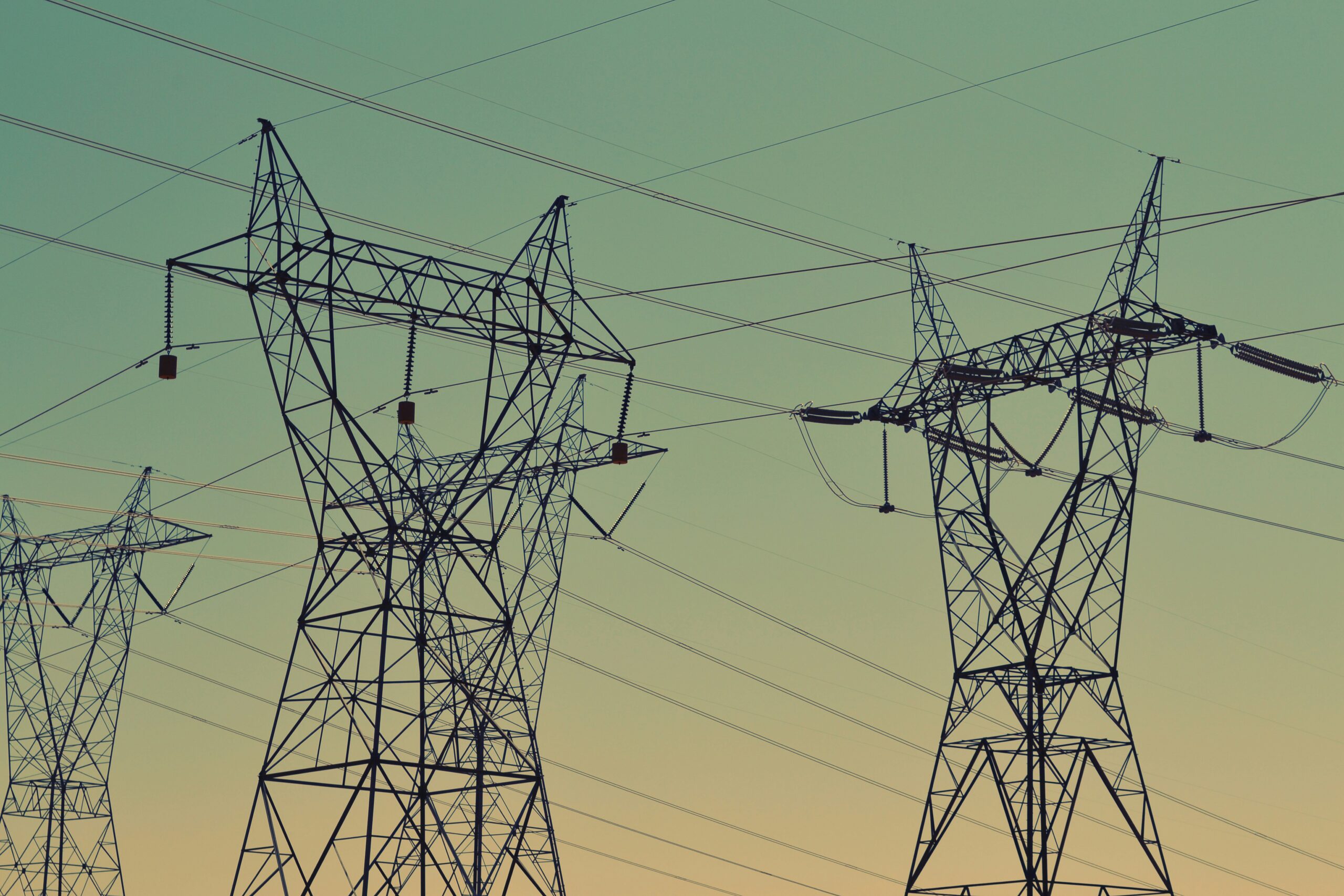 Electric power lines and transmission towers silhouetted against a dusk sky.