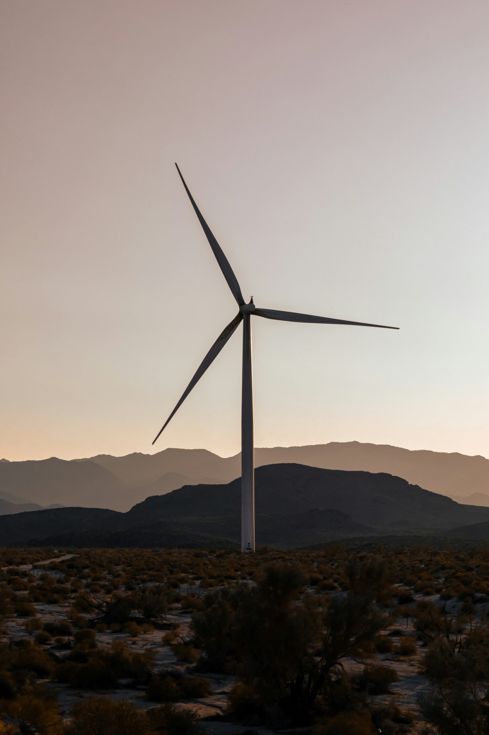 Wind turbine set against a mountain landscape during sunset, representing renewable energy.