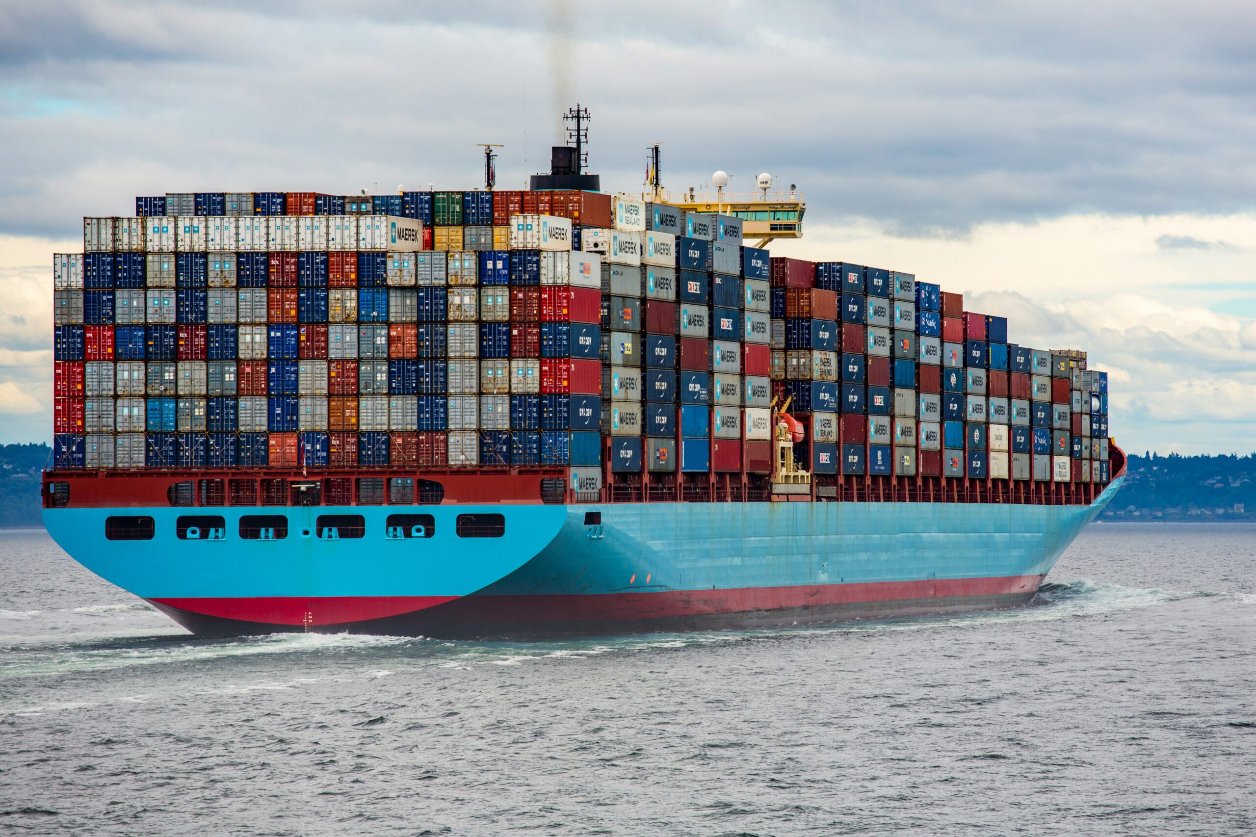 A large container ship loaded with multicolored shipping containers, transporting valuable materials like gallium, germanium, and antimony across the sea.