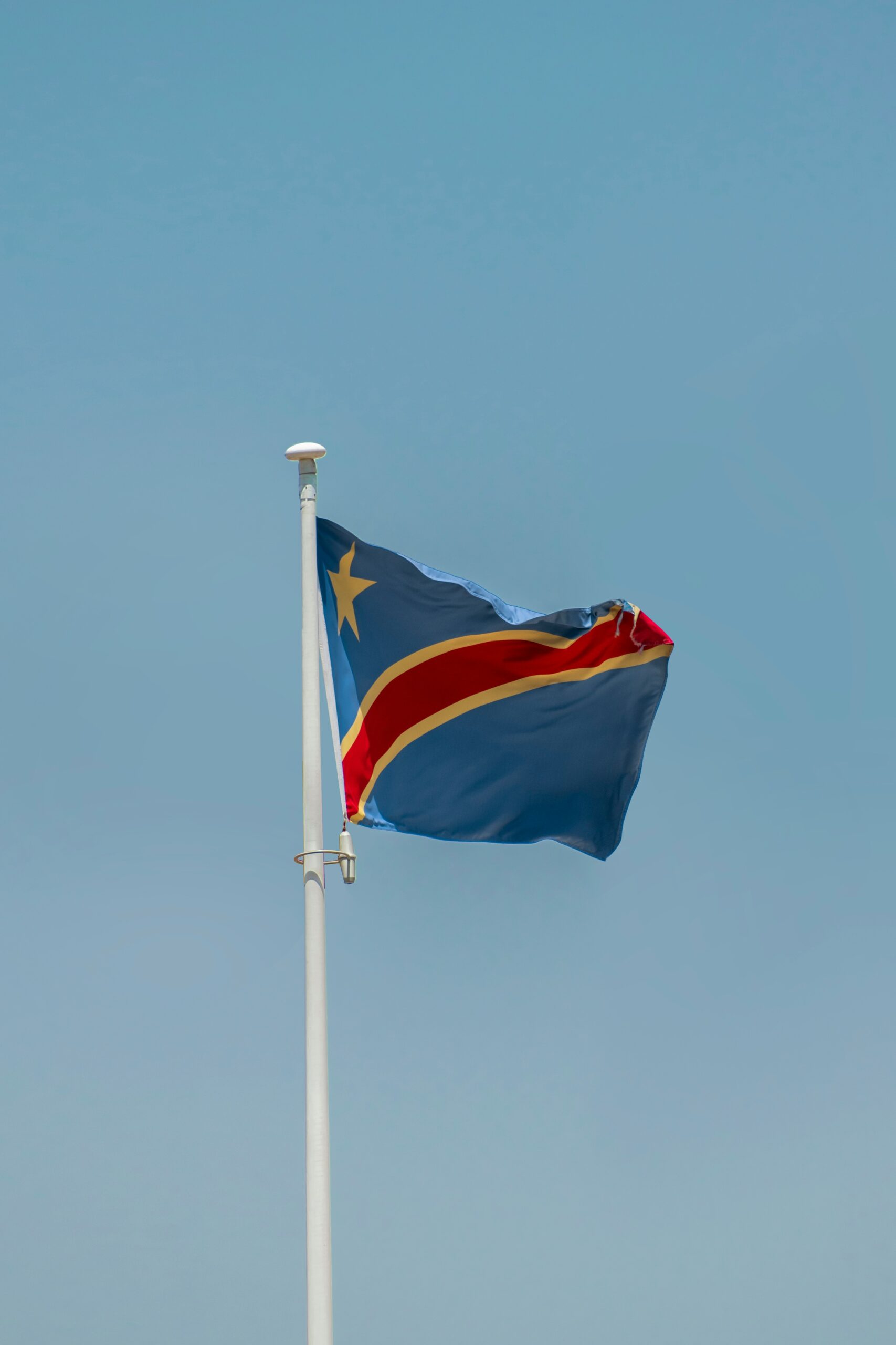 The national flag of the Democratic Republic of the Congo (DRC) waving against a clear blue sky, symbolizing the nation’s rich cobalt resources and strategic role in global supply chains amid evolving export policies.