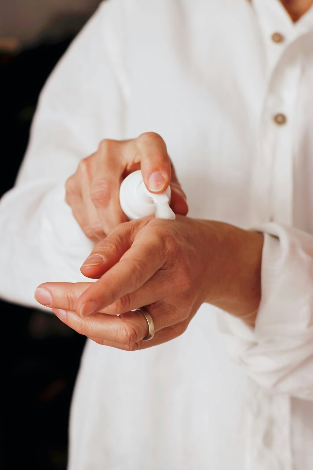 A person applying glycerin-based lotion on their hand, dressed in a white shirt.