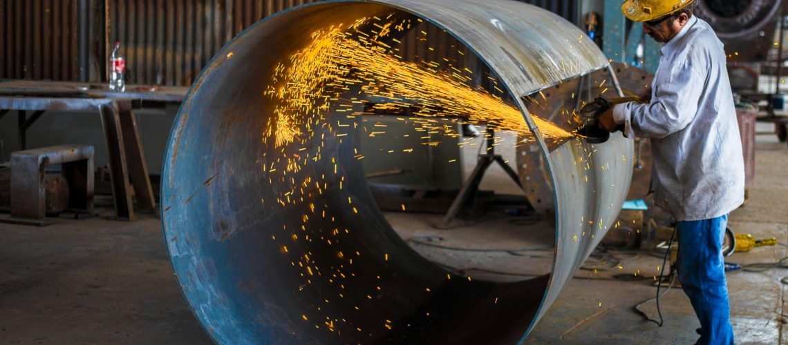 Worker using a grinder on a large metal cylinder, illustrating the industrial applications of boride compounds.