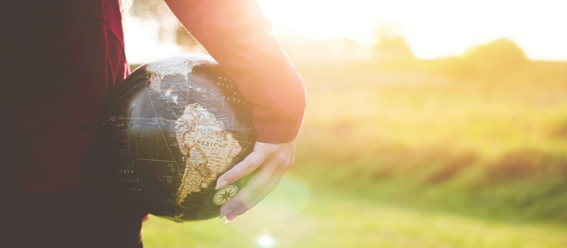 Person holding a globe in one hand, standing in a sunlit field, symbolizing global impact and sustainable energy solutions.