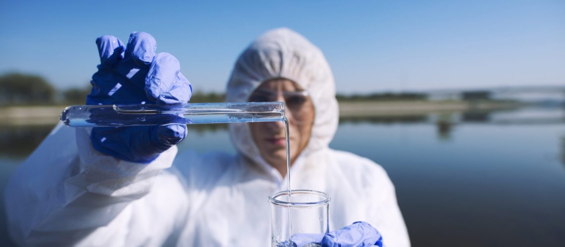 Ecologist sampling water from the river with test tube.