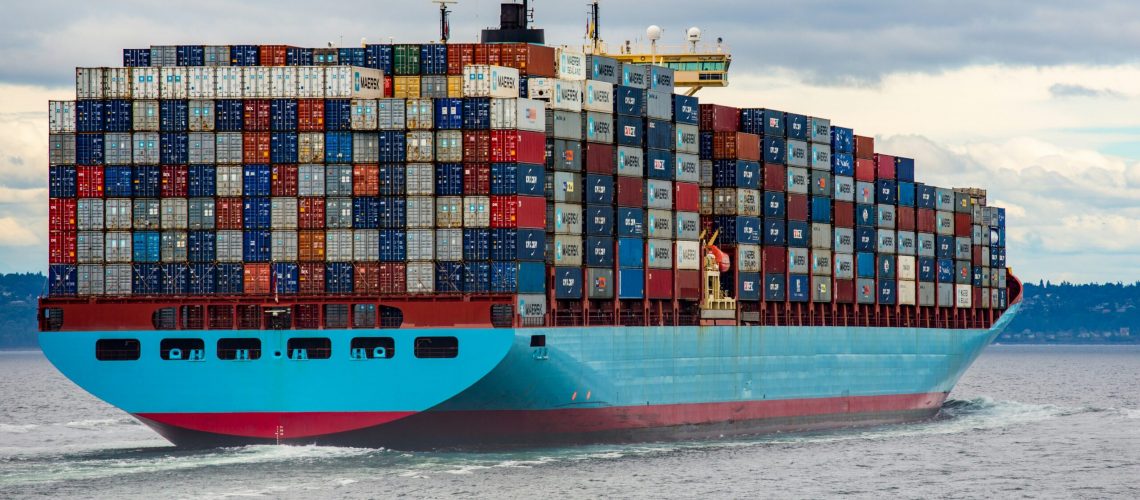 A large container ship loaded with multicolored shipping containers, transporting valuable materials like gallium, germanium, and antimony across the sea.