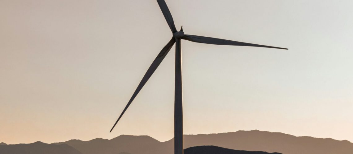 Wind turbine set against a mountain landscape during sunset, representing renewable energy.