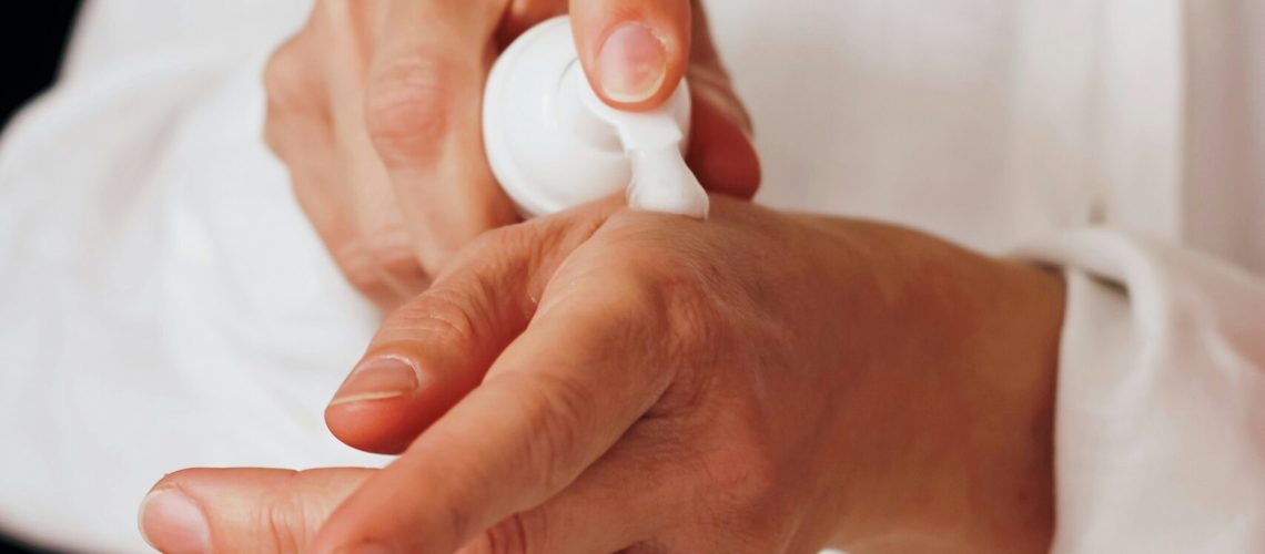 A person applying glycerin-based lotion on their hand, dressed in a white shirt.